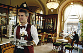Hungary, Budapest, Pest. Waiter at Gerbaud cafe and Pastries. Holding a chocolate Ice