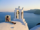 Greece. Cyclades Islands, Santorini. Vlilage of Oia. Lady havin a rest on. the roof of a white church