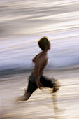 Beach boy running along water