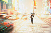 A lone figure in black with an umbrella walking in Times Square during a snow storm, traffic is blurred on either side of the person. New York City. USA