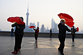 China. Shanghai. Chinese women dance with red fans on the bund in Shanghai for exercise every morning.
