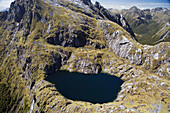 New Zealand, South Island, Fiordland National Park, Small Lake and Waterfall high in Kepler Mountains feeding Delta Burn - aerial