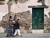 People in indigenous dress pass by decaying building on the streets of Antigua, Guatemala