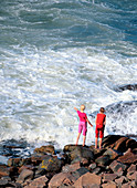 Two red-dressed girls playing on shore during windy day. Skåne, Sweden
