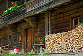 traditional farmers house with flower decoration and pile of fire wood in front, Ellmau, Kaiser range, Tyrol, Austria