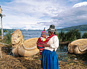 Uru indian mother and child and totora reeds boat. Titicaca Lake. Peru