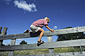 Boy climbing over a fence.