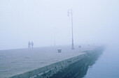 People walking along the pier in fog, Trieste, Italy