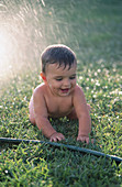 Infant boy playing with water hose in the garden