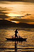 Mann paddelt stehend im Kanu bei Sonnenuntergang, Neubritannien, Papua Neuguinea, Ozeanien
