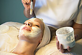 21-jährige Frau lässt sich von einer Schönheitstherapeutin eine Gesichtsmaske auftragen