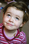 Headshot of 3 year old girl, with plaits and stripey top, looking up