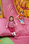 Two three year old girls sliding down a big bouncy slide.