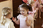 A group of 3 year old girls in ballet class, dressed in pink leotards and tights, clapping