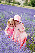 3 and 5 year old sisters standing together in a field ful of lavender, with their arms round each other