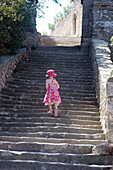 The back of a 5 year old girl in a red sundress, walking up a massive flight of ancient steps, in the sunshine