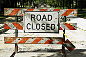 Road Closed sign posted on orange and white striped barricade, repair residential suburban neighborhood road. Riverwoods. Illinois. USA.