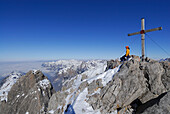 Frau sitzt am Gipfelkreuz der Mädelegabel, Allgäuer Alpen, Bayern, Deutschland