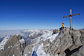 Woman sitting at summit cross of mount Madelegabel, Allgaeu Alps, Bavaria, Germany