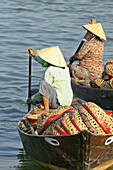 Women with baskets wait in boats on the river at the market in Hoi An.