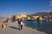 A couple walking along the promenade, Kyrenia harbour and Kyrenia castle, Kyrenia, Girne, North Cyprus, Cyprus