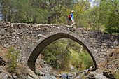 A hiker walking over a stone bridge, Elaia bridge, Diarizos Valley, near Pafos, Cyprus