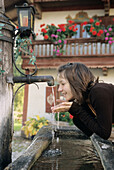 Junges Mädchen (14-15 Jahre) trinkt an einem Brunnen, Bayern, Deutschland
