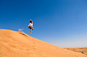 Woman jumping down a sand dune in the desert, United Arab Emirates