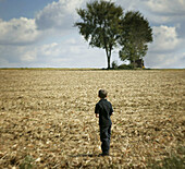 A boy looks to a copse of trees.