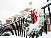 Boston, MA: Snow covers the lawn of the Massachusetts State House while a Christmas wreath decorates an iron fence in front.