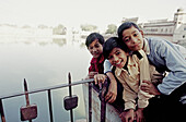 Three young Indian boys huddle together posing for the camera next to a metal fence.