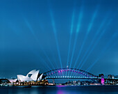 Sydney Opera House and Harbour Bridge at dusk with many spotlights on the bridge lighting upwards.