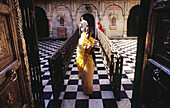 Indian woman wearing yellow sari with praying hands walking out of Rat temple or Karni Mata Temple in the village of Deshnok, near Bikaner in Rajasthan, India.