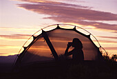 A silhouette of a woman in her tent drinking during a sunset at Smith Rock, OR.