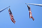 Two American flags on flagposts, being blown by the wind