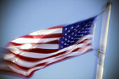 An American flag billowing in the wind against a blue sky.