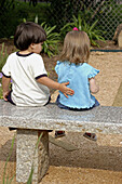 Toddler boy and girl sitting on park bench