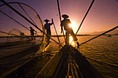 Legrower fisherman set conical traps as the setting sun reflects on Inle Lake, Shan State, Myanmar (Burma)