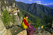 Bhutanese woman sitting on a rock overlooking the Taktshang Monastery (Tigers Nest), Paro Valley, Bhutan