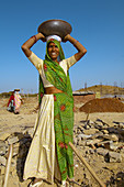 Woman breaking up and carrying rocks at a construction site, Udaipur, Rajasthan, India