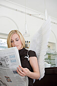 Angel, young woman with wings reading a newspaper in a cafe, Munich, Bavaria, Germany