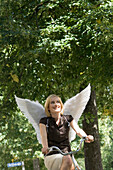 Mid adult woman wearing angel wings riding a bicycle