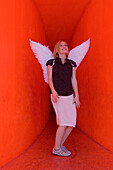 Frau mittleren Alters mit Engelsflügeln in einem rotem Tunnel