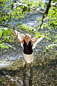 Mid adult woman wearing angel wings standing in lake Starnberg spraying water, Bavaria, Germany