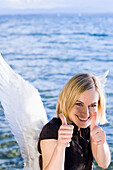 Mid adult woman wearing angel wings showing thumbs up