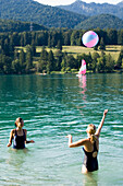 Zwei junge Frauen spielen im Walchensee mit einem Ball, Bayern, Deutschland