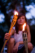Young woman lighting a torch on the banks of the river Isar in the evening, Munich, Bavaria, Germany