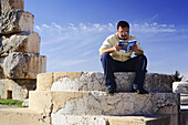 Man reading travel guide on steps of Roman temple, Baalbek, Lebanon