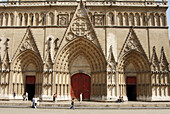 Close up of three entrance doors at St. Jean Cathedral, Lyon, France. Pedestrians walking by.