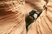 Female canyoneer stemming across a sandstone slot in Pritchett Canyon near Moab, Utah, USA